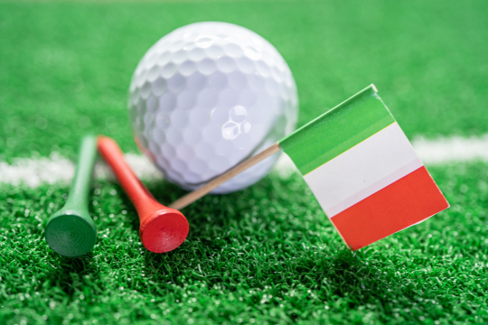 Golfball liegt im Gras mit einer Italien Flagge und einem grünen und roten Golftee